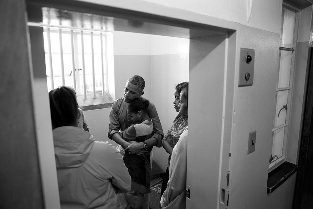 President Barack Obama and First Lady Michelle Obama, along with daughters Sasha and Malia, stand in former South African President Nelson Mandela's cell as they listen to former prisoner Ahmed Kathrada during their tour of Robben Island Prison on Robben 